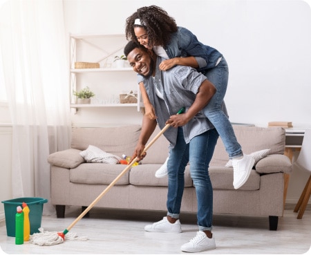 Een man draagt een glimlachende vrouw op zijn rug terwijl hij een mop vasthoudt in een schone kamer.